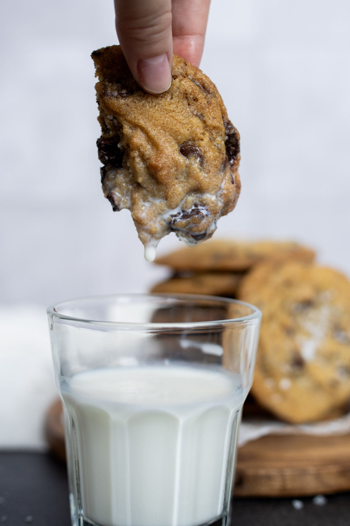 Half of a chocolate chip cookie being dipped in a glass of milk