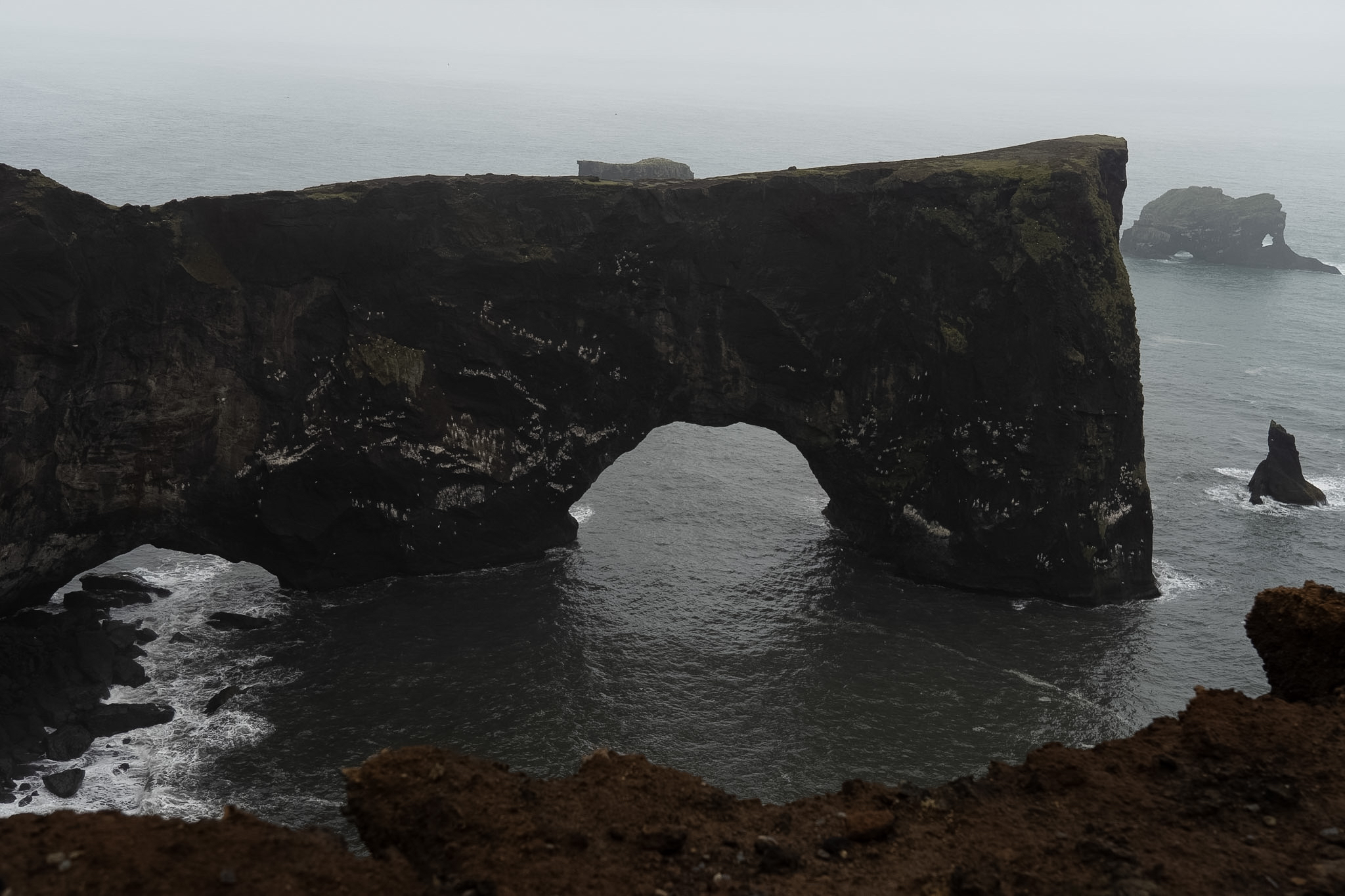 Massive coastal rock arch in misty ocean